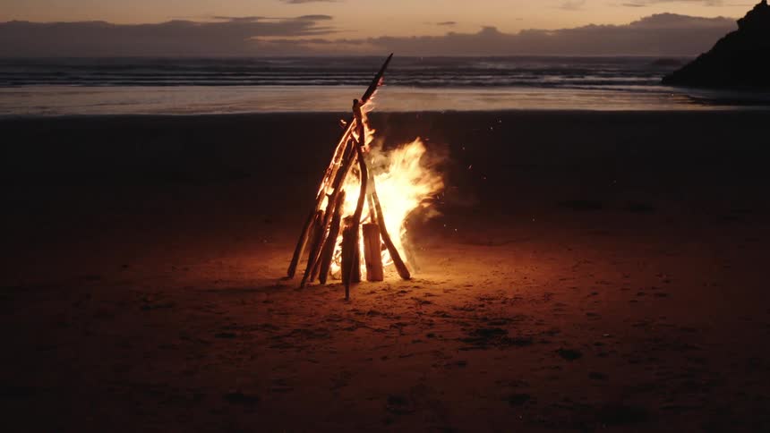 A bonfire burning on a beach at sundown