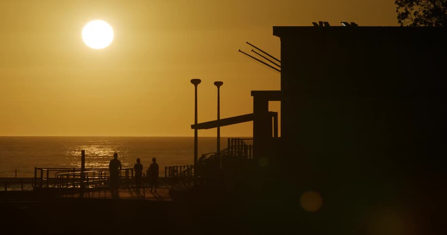 People walking away from the pier and the ocean at sunset
