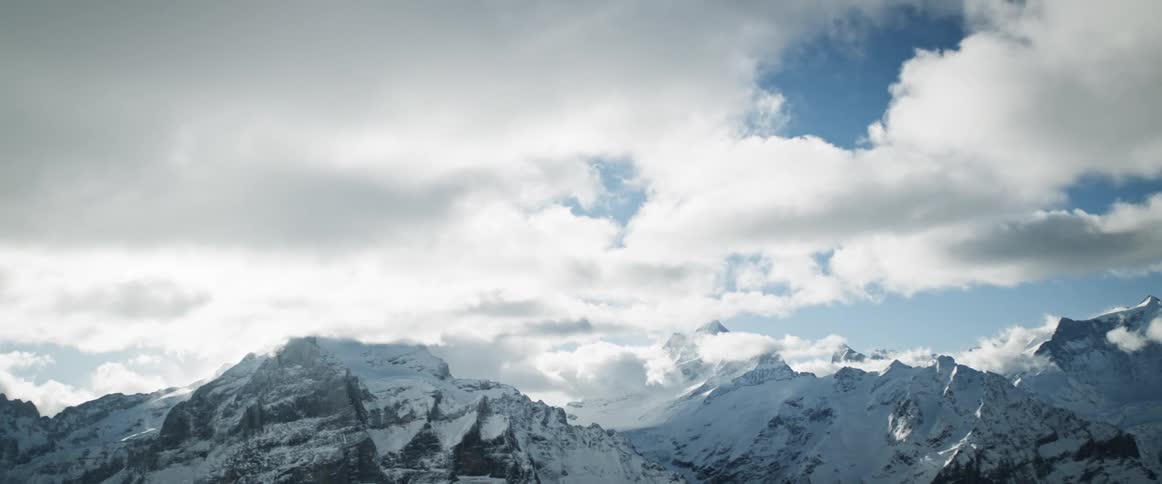 Snowy mountains tower over snow covered plain on a heavily clouded day