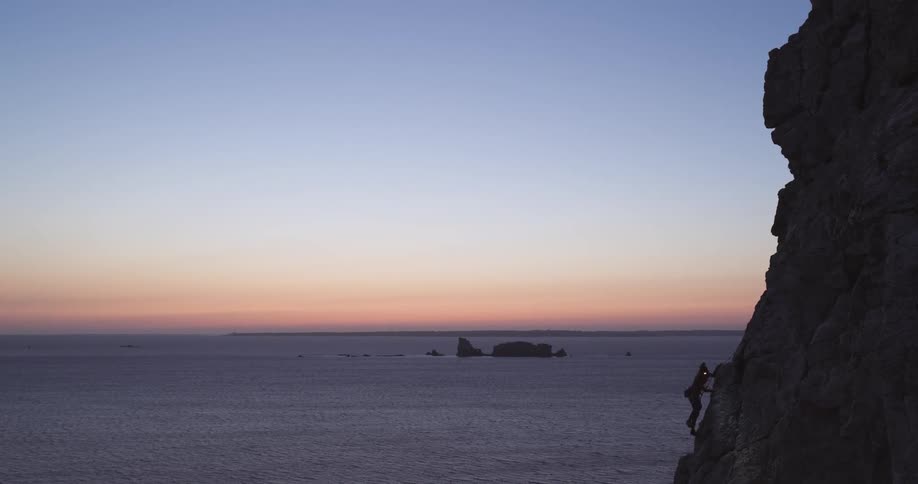 A man is rock climbing at sunset