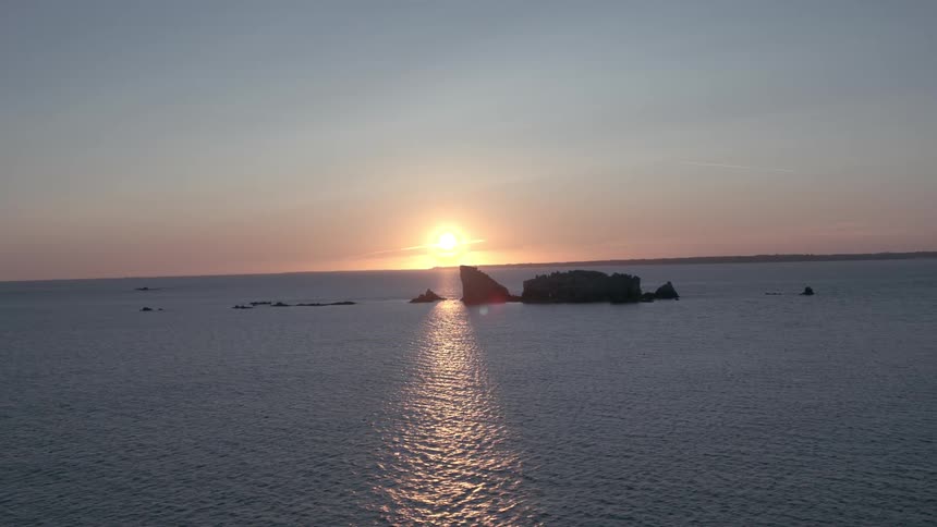 Jagged rocky islands in the middle of the ocean with the sun setting behind them