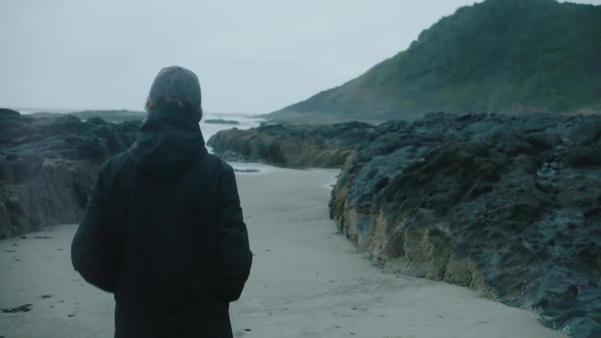 A man walks on a narrow beach