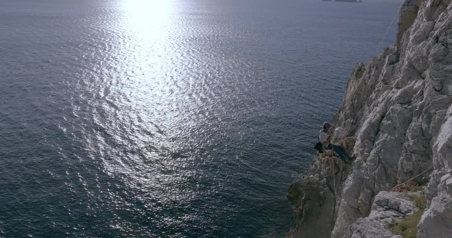 Man rappels down a rocky cliff at the ocean