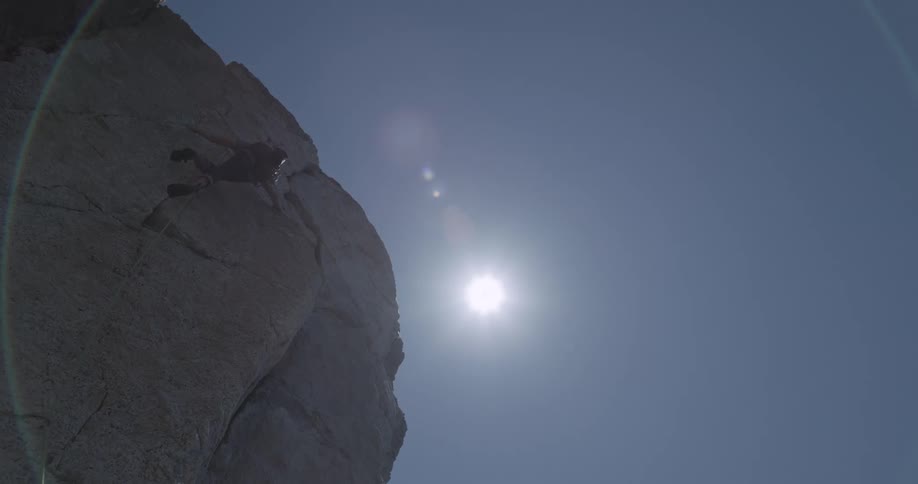 Man climbing and climbing the rocky wall of a mountain on a sunny cloudless day