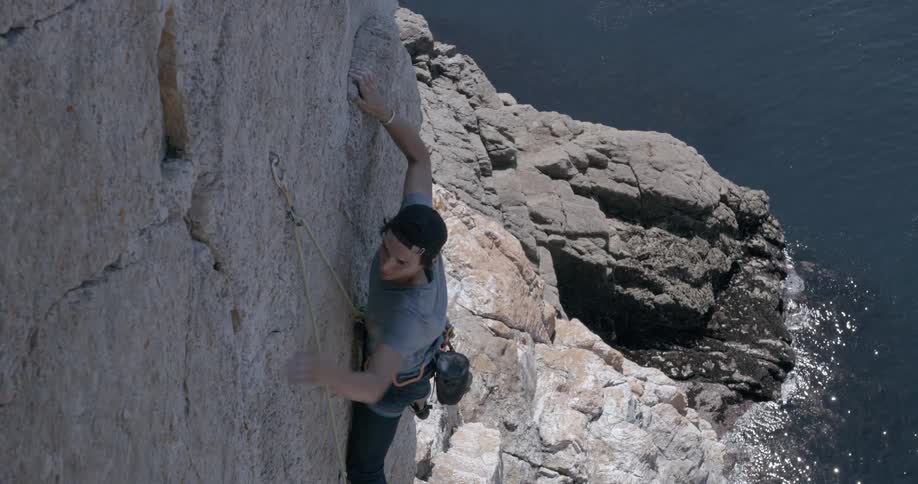 Man with safety belts and ropes climbing the rocky wall of a mountain by the sea
