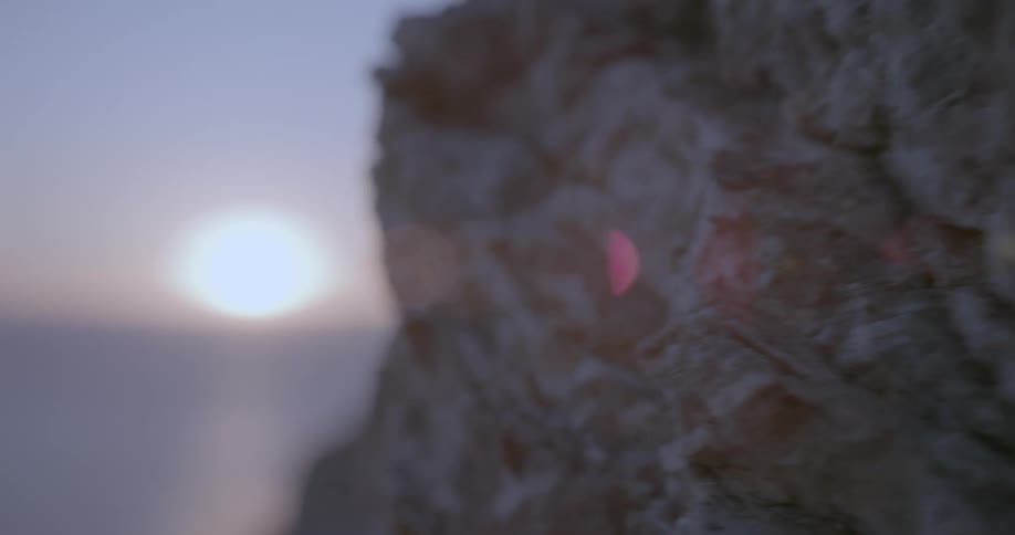 Closeup on a rocky mountain with a sun on the horizon next to the sea