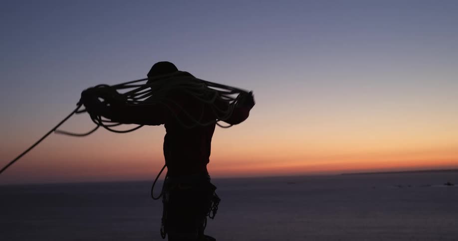 A man wraps up some rope at sunset