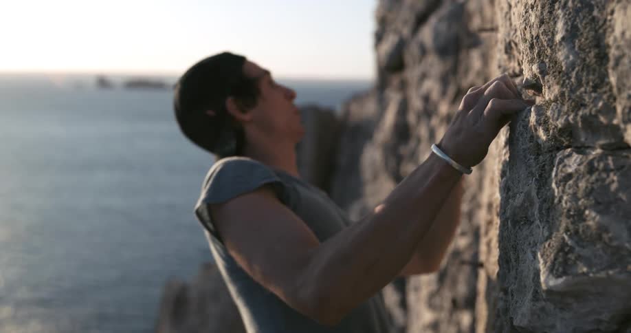 Man climbing a rocky wall of a mountain by the sea
