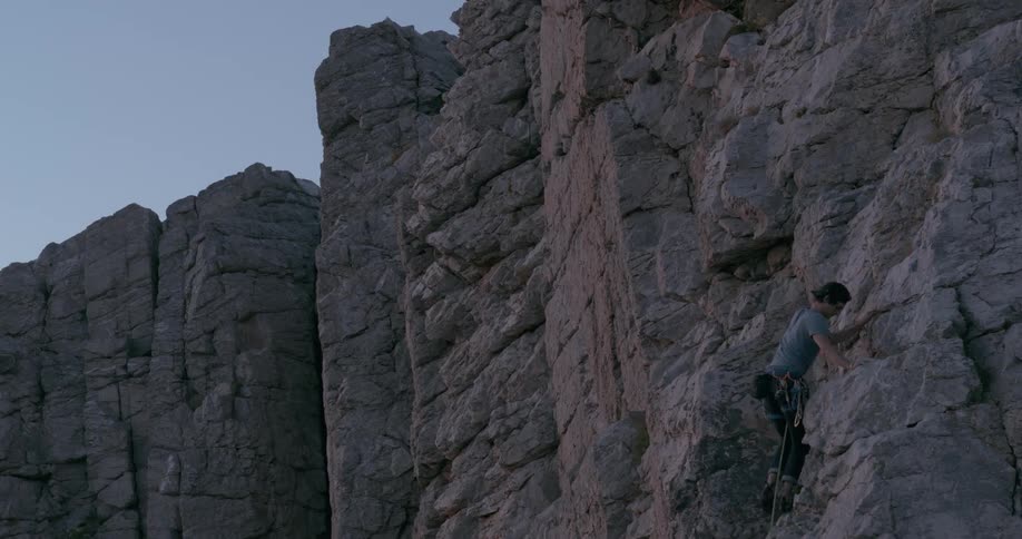 A person is rock climbing on a steep rugged cliff during the evening