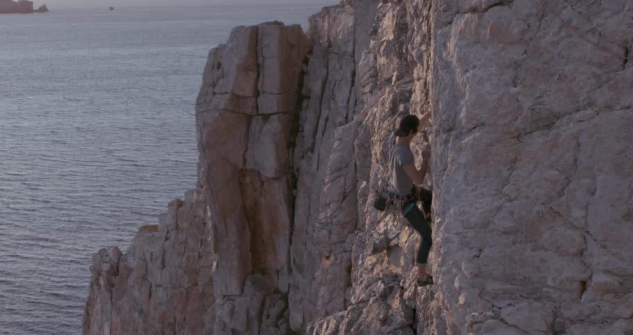 A man climbs a steep cliff near the ocean