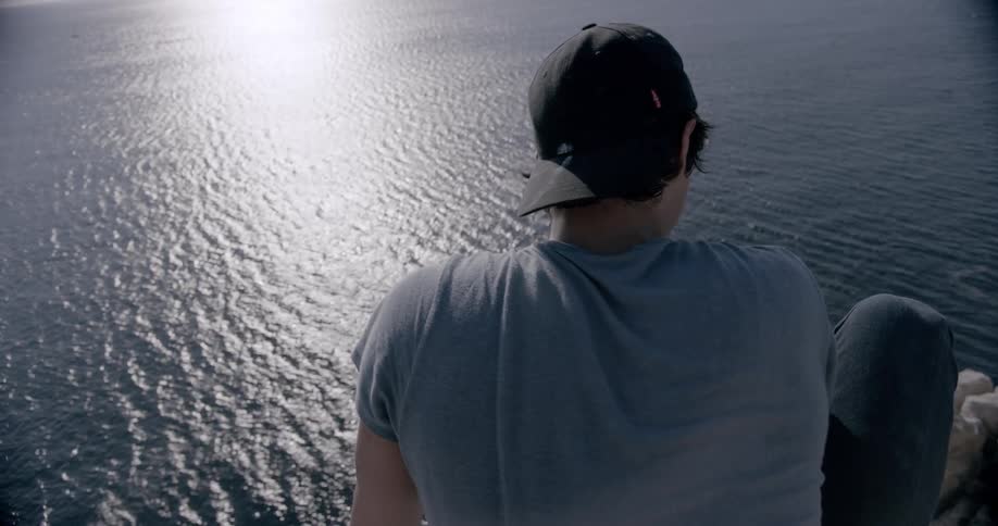 A person is looking at a sunlit ocean from a high cliff