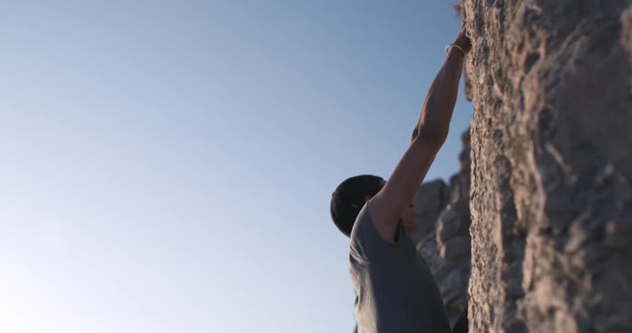 A person is climbing a rock and is wearing a cap facing backwards