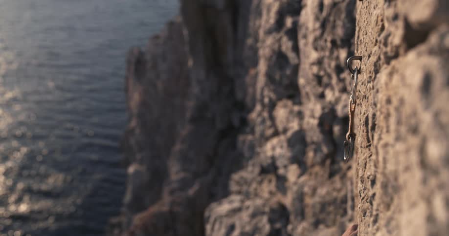 Hands of a man nailing a stake and a safety rope to a mountain wall on a seaside cliff
