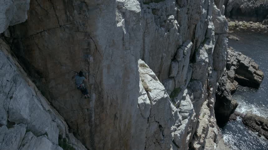 Man climbing a huge rock wall of the seaside coast on a cloudy sky day