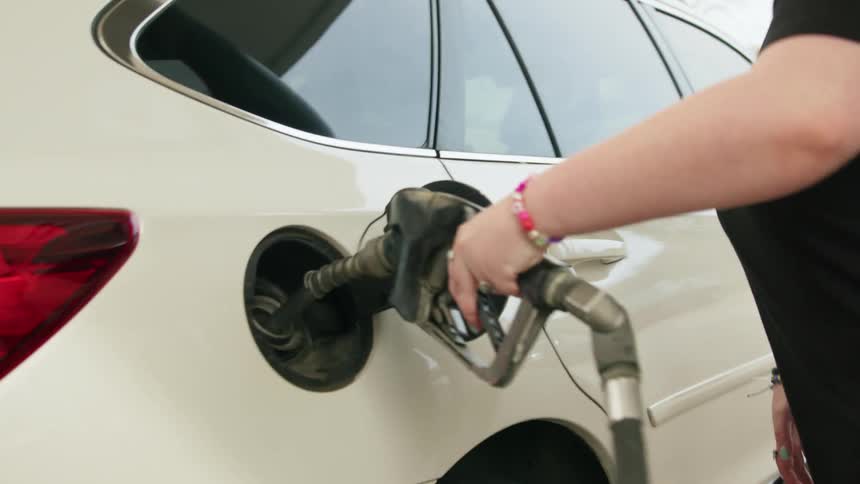 Woman puts gas pump into gas tank of vehicle at gas station