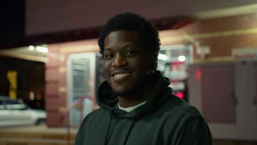 Man turns and smiles in front of a convenience store