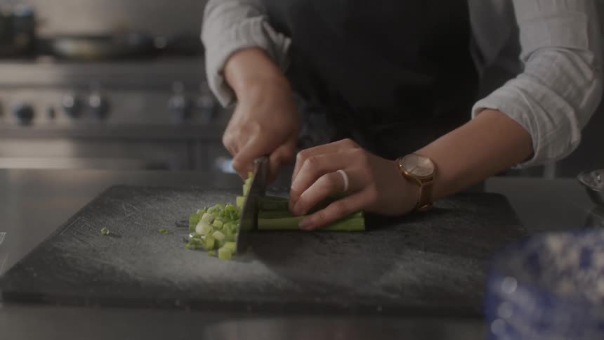 A woman chops celery evenly on a cutting board