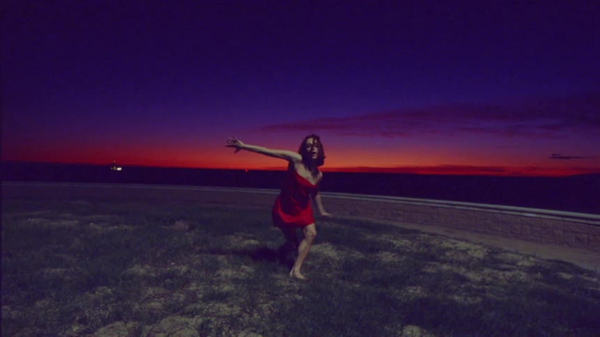 Woman in a red dress dancing on grass on a dark reddish sky