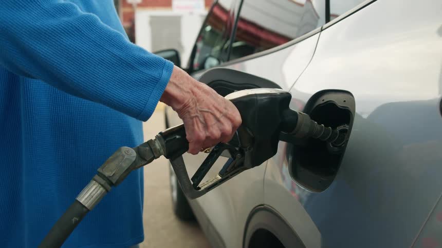 Elderly woman places the pump into the gas tank inlet of her silver car