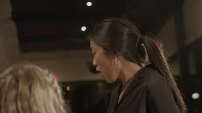 An asian server smiles and laughs while serving patrons