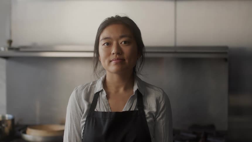 Portrait of a young asian woman in the kitchen and wearing a black apron
