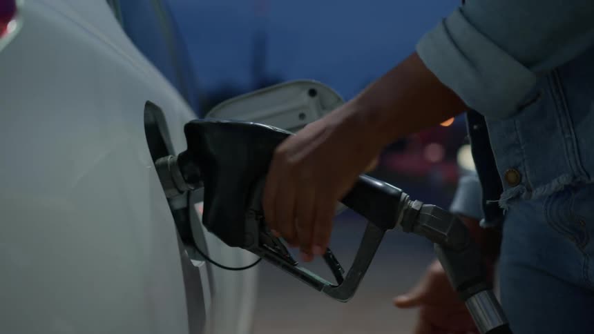 Closeup of a womans hands nailing the gas station pump valve and placing it in the car