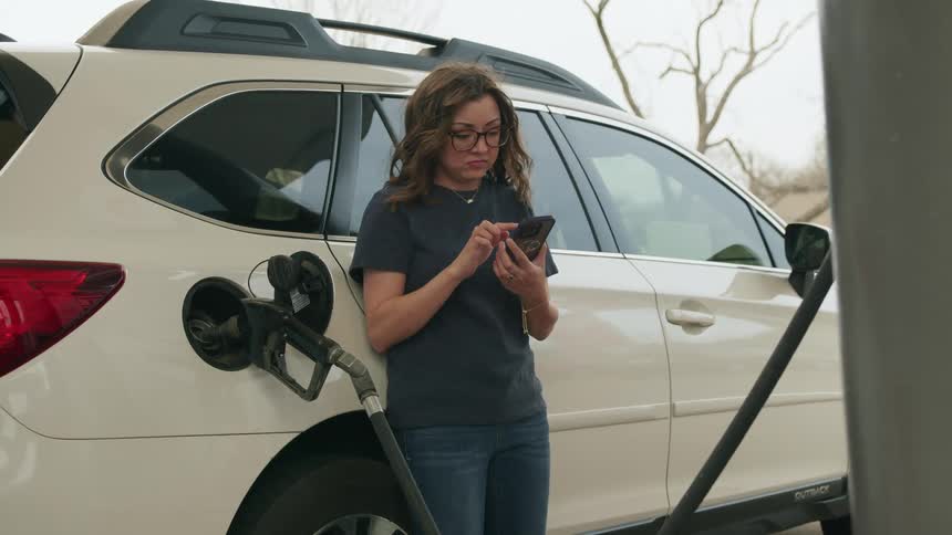 A woman scrolls her phone while pumping gas