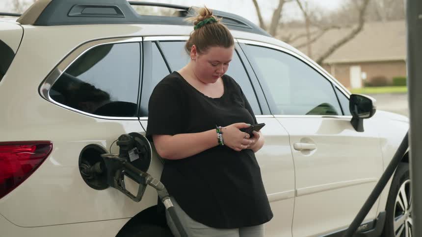 A woman scrolls her phone while pumping gas