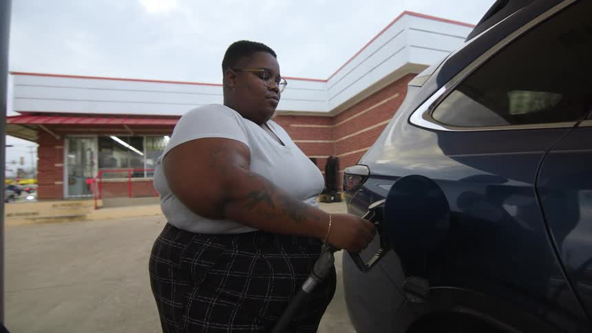 Woman looks behind her while putting gas in her car to check the progress of the fueling on the pump