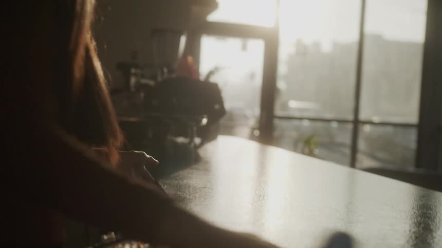Young woman wiping with a cloth the countertop of a restaurant with a reflection of sunlight during the day