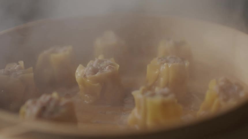 Savory asian dumplings being steam cooked in a wooden bowl