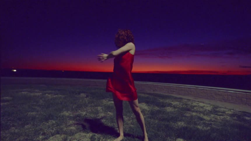 Redheaded woman wearing a red dress dances in field at night