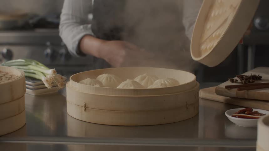A womans hands in a kitchen taking a large bowl and opening it with steamed nukiman dumplings