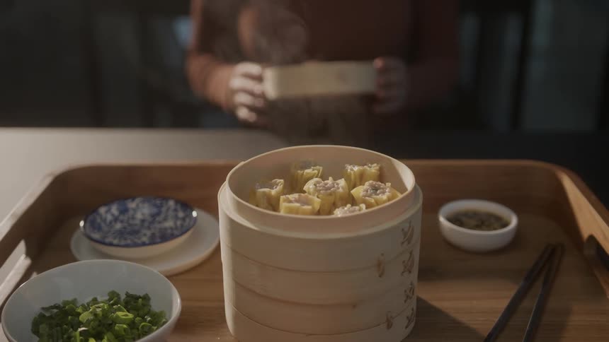 Closeup of a womans hands removing the lid from a bowl of steambaked dumplings in an asian cuisine presentation