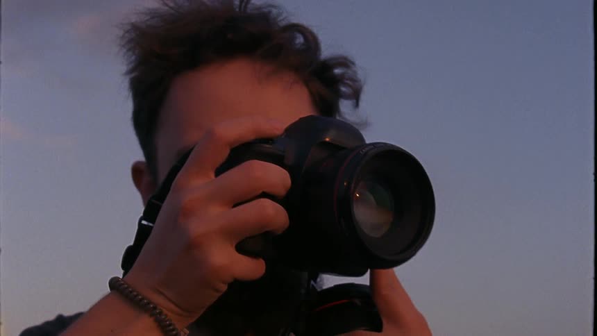 Male photographer takes picture with camera while standing outdoors on a windy day