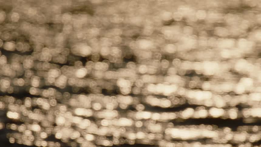 Blurry points of light reflect off ocean waves during sunset