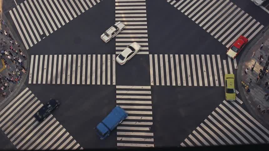 Intersection with vehicle traffic in a metropolis with pedestrians waiting on the sidewalks to cross