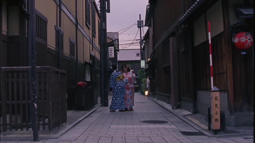 Japanese residential neighborhood in an alley with three women in front of a small shrine in kimonos