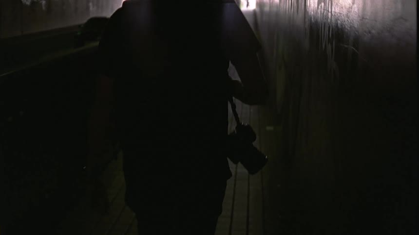 Back view of a man walking on an overpass carrying a professional camera on his waist