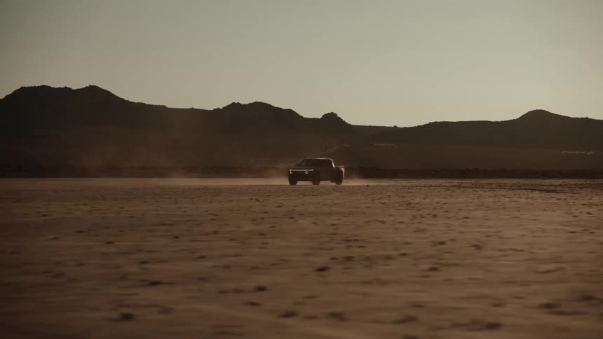 A truck drives in the desert past the mountains