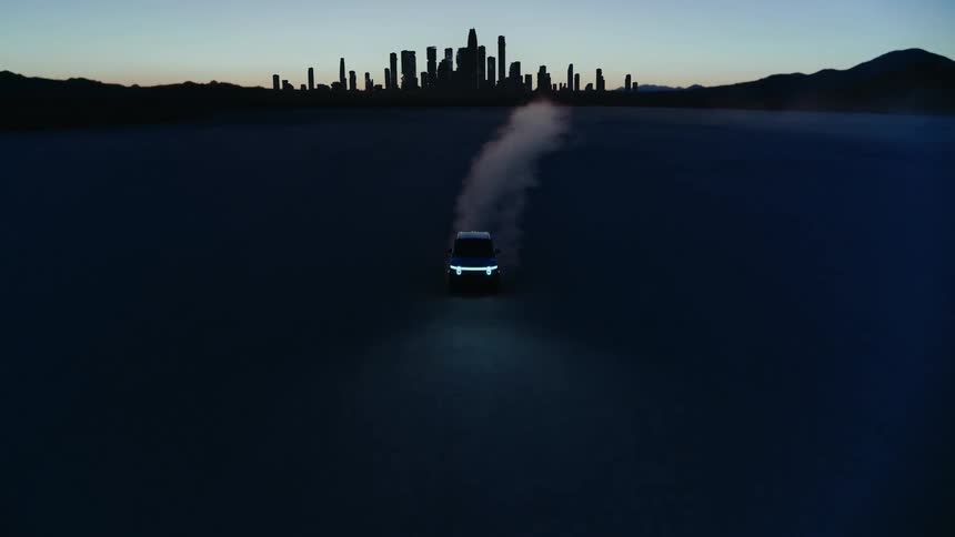 Car speeding along a desert road in the morning with the silhouette of a city and mountains on the horizon