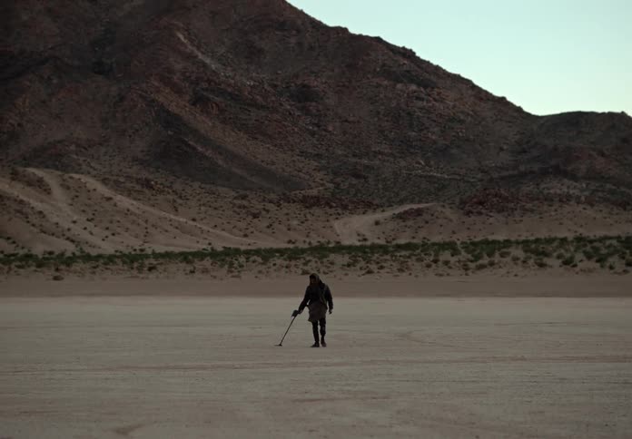 A man uses a metal detector in a desert