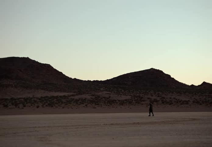A man walking through the desert a sunrise with a metal detector