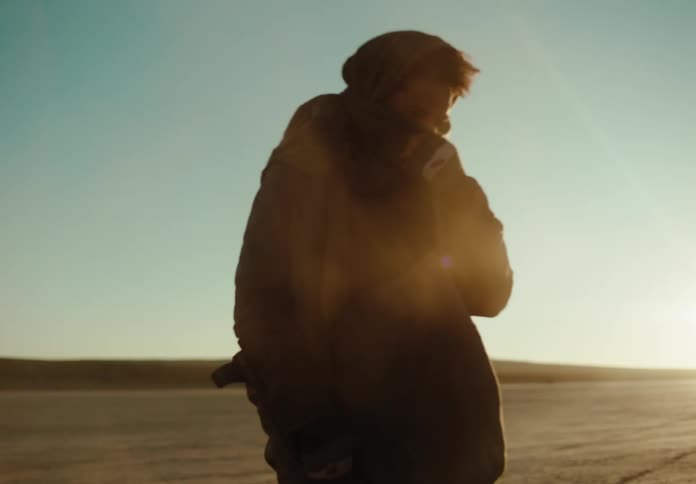 A man in the desert holding a metal detector removes his protective mask
