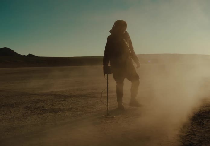 A man is running a metal detector through the desert