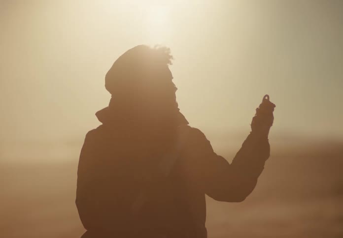 Silhouette of a man finding a metal object on dry soil in the desert on a bright sunny day