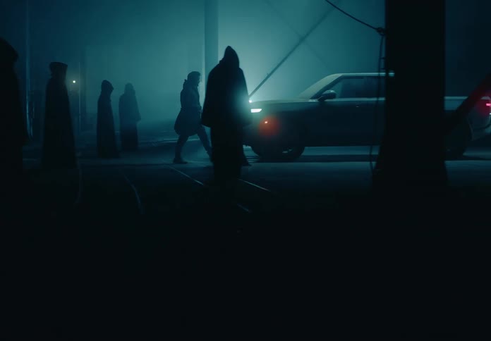 A man walks through a group of people wearing cloaks with hoods to get to his truck