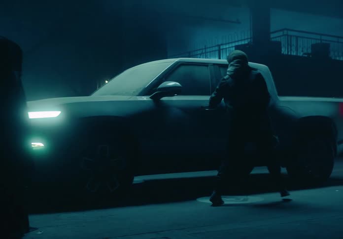 A man in a garage walks past hooded figures to get to a pick up truck covered in sand then enters it