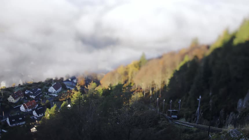 A cable car passing on a track on the right side and on the left side left left left to some houses in a rural region and there are many trees around