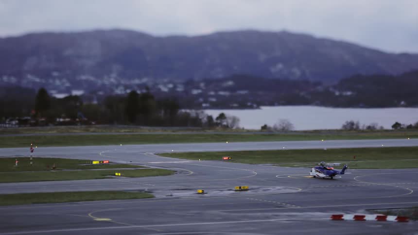 Helicopter making a turn on an airstrip next to a lake and with mountains on the horizon